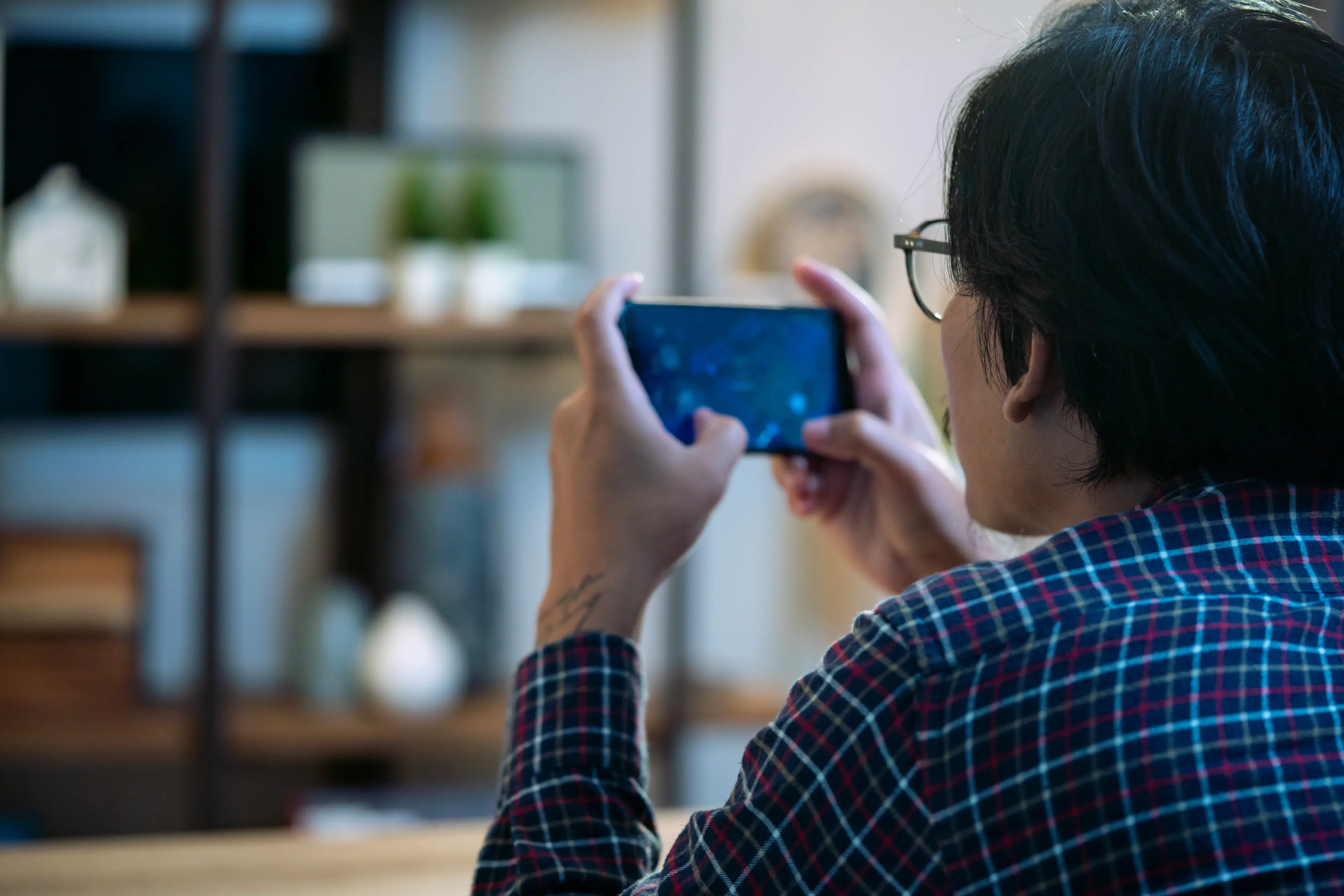 Person in plaid shirt looking at a smartphone screen, indoors.